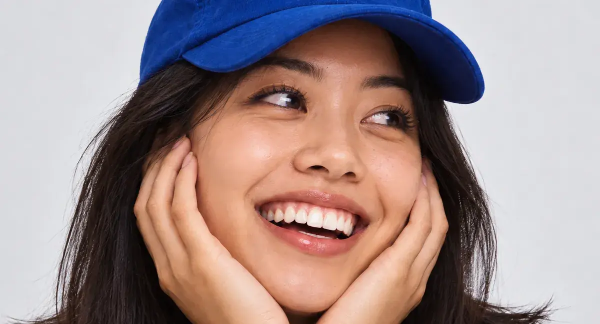 A woman in a blue cap, smiling, her chin in her hands